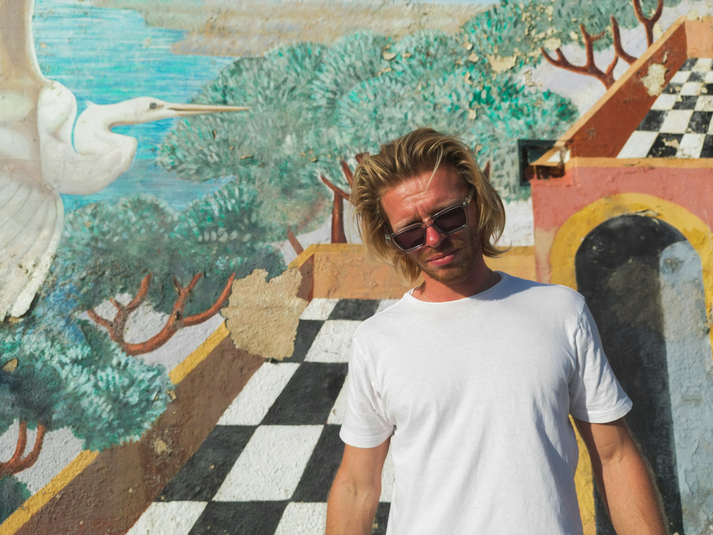 Logan Voss in a white t-shirt standing before a colorful mural in Los Angeles